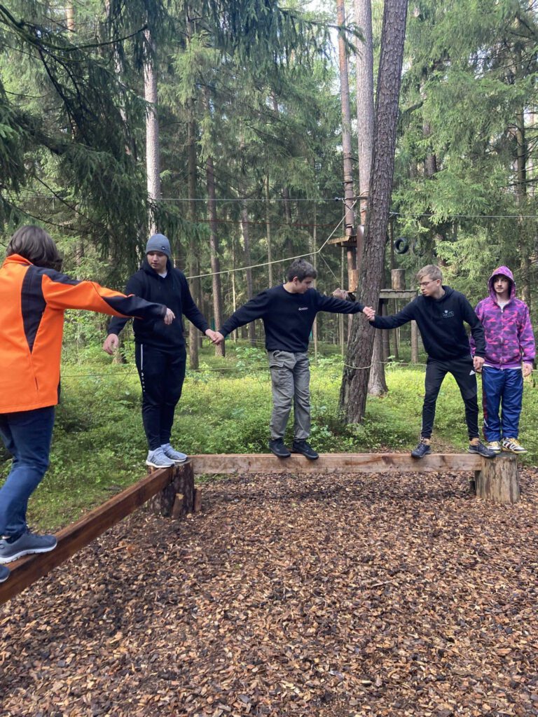 Menschen balancieren auf Balken, halten sich an der Hand